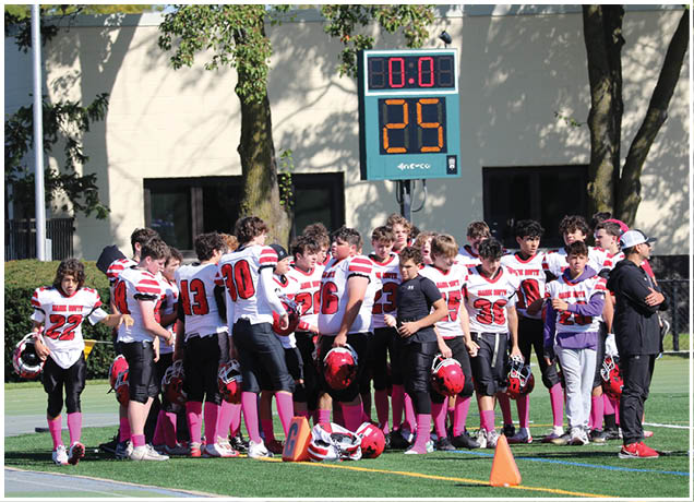 A group of people wearing sports uniforms with pink socks are gathered on a field near a scoreboard displaying a countdown. Description generated by AI