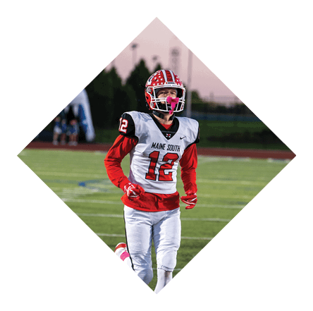 A person wearing a red and white football uniform with the number 12 is running on a green football field during dusk. Description generated by AI