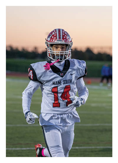 A person wearing a football uniform with the number 14 and a helmet is running on a field during sunset. Description generated by AI