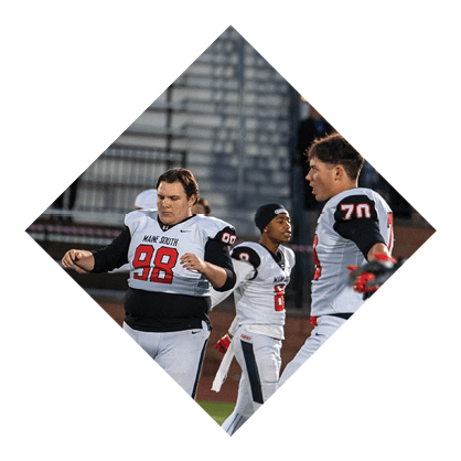 A person in a white and black sports uniform with red accents is reaching out with a gloved hand during an outdoor sports event. Description generated by AI