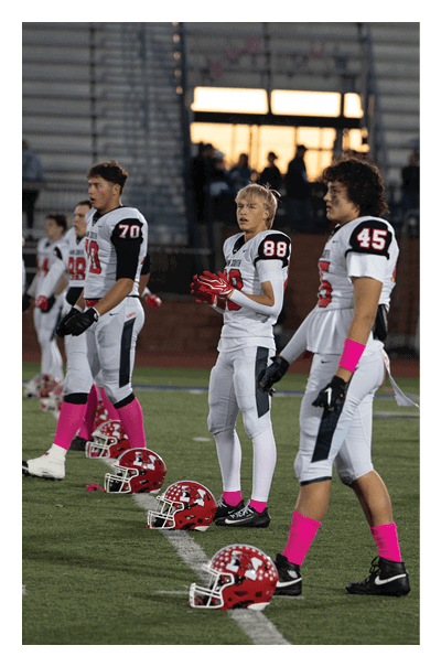 A person wearing a sports jersey with the number 70 is standing in front of empty bleachers with a few other people in the background. Description generated by AI