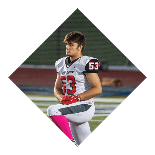 Person wearing a sports jersey stands on a field with a focused expression against a blurred background. Description generated by AI