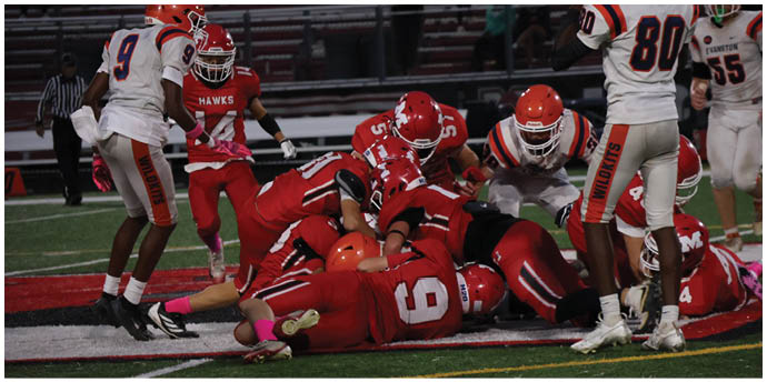 Several football players in red uniforms are piled on the ground during a game while players in white and orange uniforms stand nearby. Description generated by AI