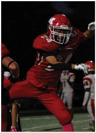 A person in red football gear is in mid-action on a field at night with other players in the background. Description generated by AI