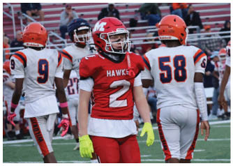 Several people wearing football uniforms are standing on a field with bleachers and spectators in the background. Description generated by AI