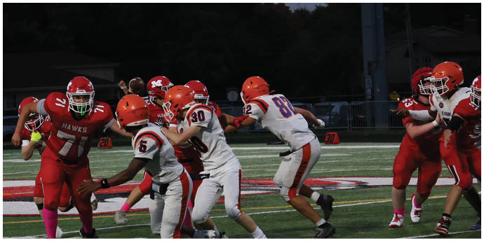 A group of people wearing football helmets and uniforms are actively playing on a field during a game at dusk. Description generated by AI