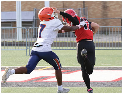 A person wearing a red and black sports uniform is running on a field with one leg bent backward. Description generated by AI