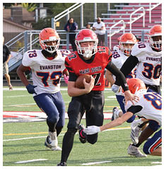 Two people in football uniforms are on a field with one holding a football and the other running behind. Description generated by AI
