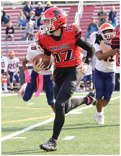 A person in a white and blue football uniform with the word Evanston is running on a football field while several people in similar uniforms stand in the background near the bleachers. Description generated by AI