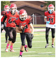 Four people in red football uniforms with helmets are running on a field, with one person holding a football and others following behind. Description generated by AI