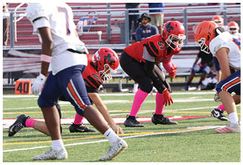 People in football uniforms are positioned on a field preparing for a play during a game. Description generated by AI