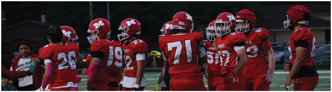 People wearing red football uniforms are standing on a field, some holding helmets, with a few people in casual clothing nearby. Description generated by AI