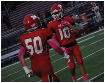 Two people in red football uniforms with pink accessories are on a football field during a game or practice. Description generated by AI