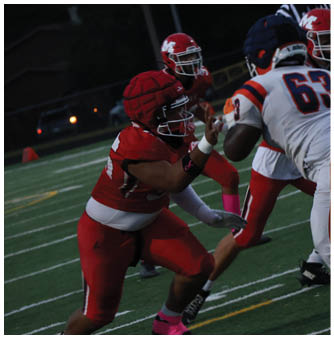 Two people in red football uniforms are playing defense against two people in white football uniforms on a field during a game. Description generated by AI