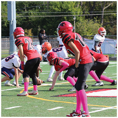 People wearing helmets and sports uniforms are positioned on a football field preparing for a play during a game. Description generated by AI