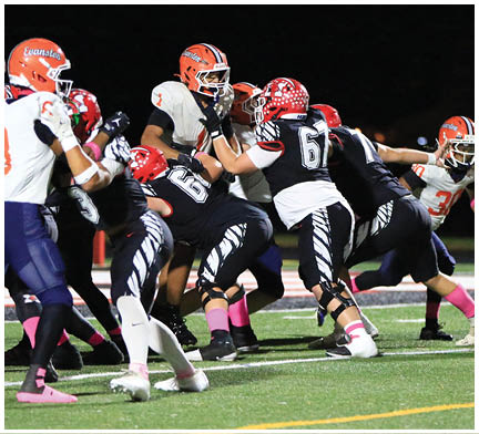 People wearing football uniforms with orange and red helmets are actively engaged in a nighttime game on a green field with white and yellow markings. Description generated by AI