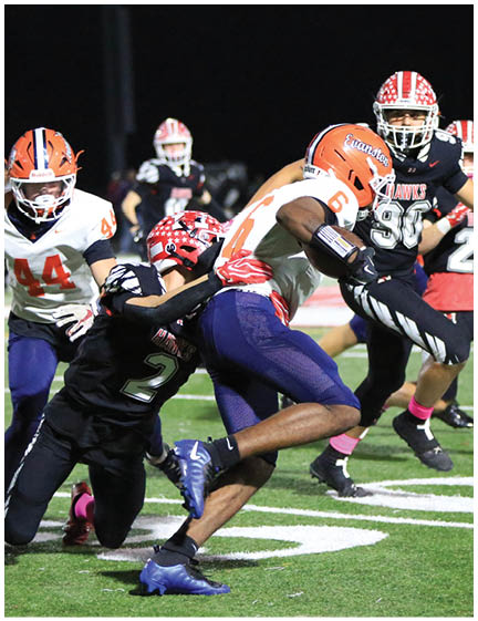 A person in a white and orange football uniform is running with the ball while another person in a black uniform with a red helmet attempts to tackle them on a football field. Description generated by AI