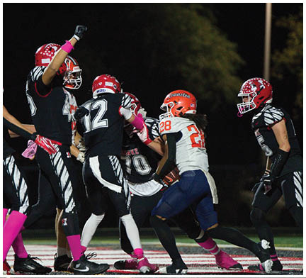 People wearing football uniforms and helmets are engaged in a play on a field at night. Description generated by AI