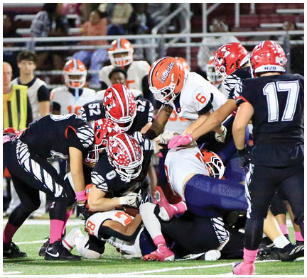 Several people wearing football uniforms and helmets are engaged in a close tackle on a grassy field during a game. Description generated by AI