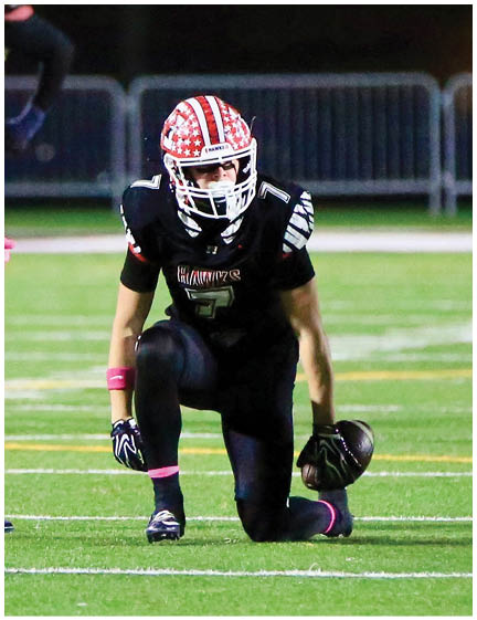 A person wearing a football helmet with a red, white, and blue star pattern is looking downward against a dark background. Description generated by AI