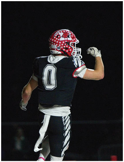A person wearing a black football uniform with the number zero and a red helmet decorated with white stars is raising one arm in a celebratory gesture on a dark field. Description generated by AI