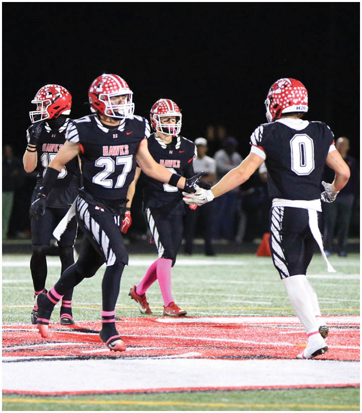 Four people in black football uniforms with red helmets are on a field at night, with two of them giving a handshake. Description generated by AI