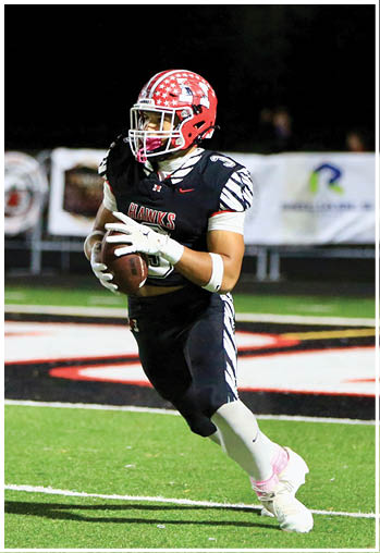 A person wearing a red helmet and black football uniform is running on a football field while holding a football. Description generated by AI