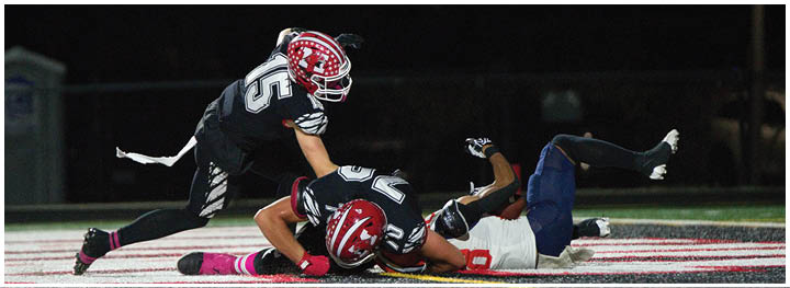 Two people in football uniforms are on the ground in an athletic field while a third person in a football uniform is reaching toward them. Description generated by AI