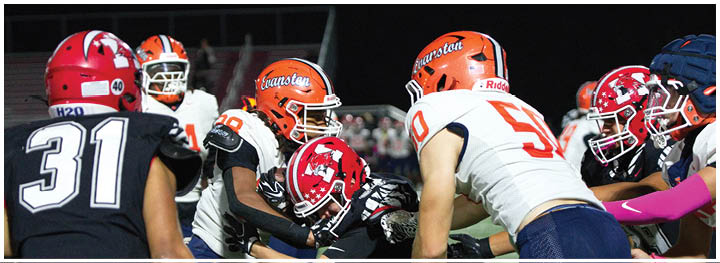 Several people wearing football helmets and uniforms are engaged in a play on a football field during a game. Description generated by AI