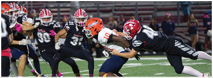 People in football uniforms are actively engaged in a tackle during a game on a field. Description generated by AI