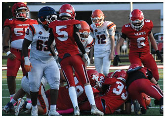 Adults in football uniforms from two teams are engaged in a play on a field with some players standing and others on the ground. Description generated by AI