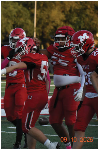 Three people wearing red football uniforms and helmets are standing together on a field with trees in the background. Description generated by AI