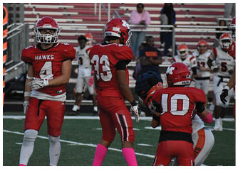 Three people in red football uniforms with helmets stand on a field with blurred spectators in the background. Description generated by AI