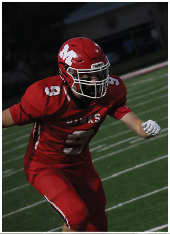 A person in a red football uniform and helmet is running on a green football field at night. Description generated by AI