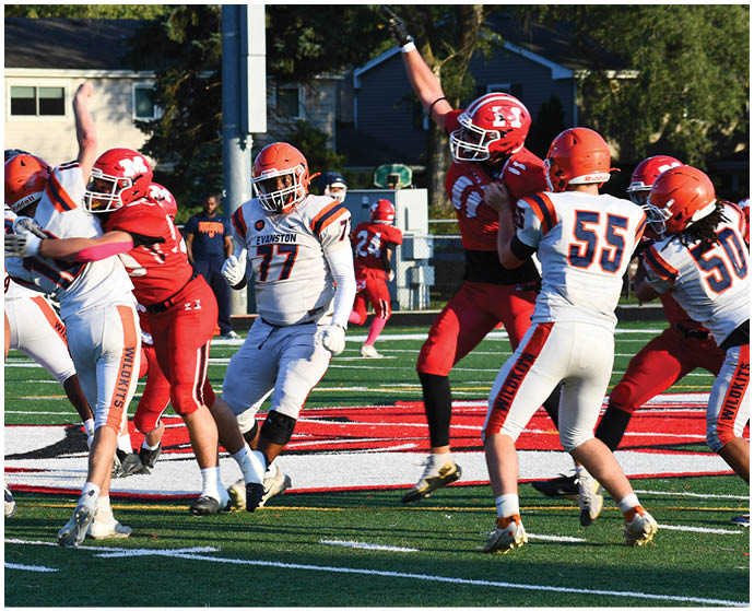Players in orange and white uniforms are actively engaged in a football game against players in red uniforms on a green field with a red and white logo. Description generated by AI