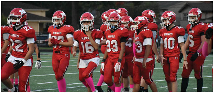 A group of people wearing red football uniforms with helmets and pink socks are walking together on a football field. Description generated by AI