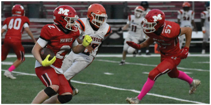 Three people in football uniforms are actively playing on a field with two wearing red and one wearing white, with one red-uniformed player holding a football. Description generated by AI