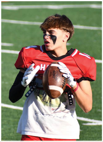A person wearing a red football uniform and black eye paint is holding a football on a green field. Description generated by AI