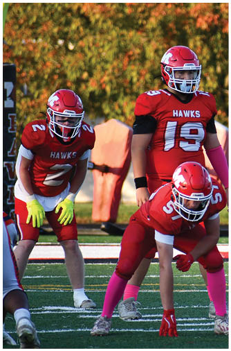 Several people in football uniforms are positioned on a field preparing for a play during a game. Description generated by AI