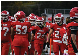 Several people wearing red football uniforms and helmets with the word “HAWKS" are standing together on a field. Description generated by AI