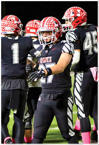 A person wearing a red and white star-patterned football helmet and a black jersey with “HAWKS" written on it is on a football field at night. Description generated by AI