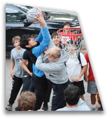 A group of people are playing basketball outdoors with one person jumping to shoot the ball while others watch or try to block near the hoop. Description generated by AI