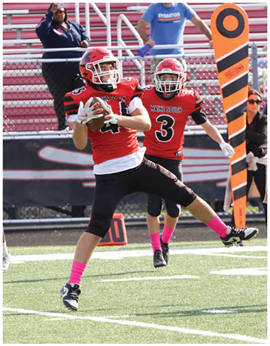 Two people in red football uniforms with pink socks are actively playing on a football field near an orange yard marker. Description generated by AI