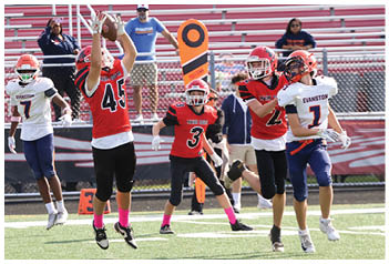 People wearing football uniforms from two different teams are jumping and running on a football field during a game. Description generated by AI