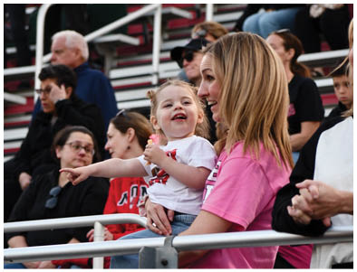 Adults and children are seated in a stadium with red and white bleachers in the background. Description generated by AI