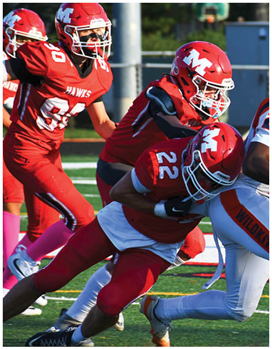 A person wearing an orange and white football uniform is running with the ball while two people in red uniforms attempt to tackle them on a football field. Description generated by AI