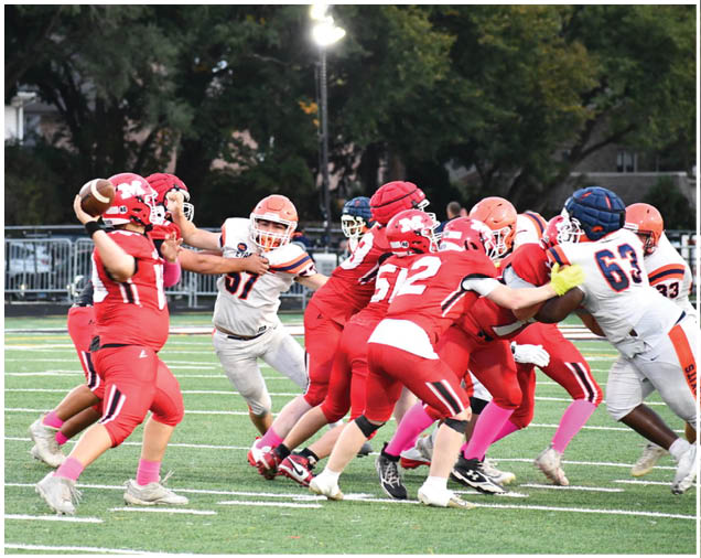 A group of people in red and white football uniforms are actively engaged in a play on a green field under stadium lights. Description generated by AI