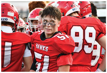 A group of people wearing red football uniforms with helmets, one person in the center with face paint and the number 51 on their jersey looking slightly to the side. Description generated by AI