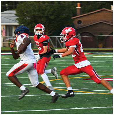 Three people in football uniforms are actively running on a field with one person in white and two in red chasing or defending. Description generated by AI