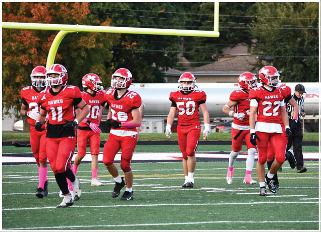 A group of people wearing red football uniforms with helmets are walking on a football field near a goalpost. Description generated by AI